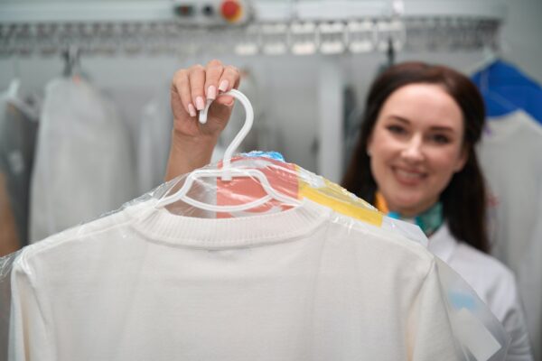 Woman administrator of laundry office holding hanger with white t-shirt